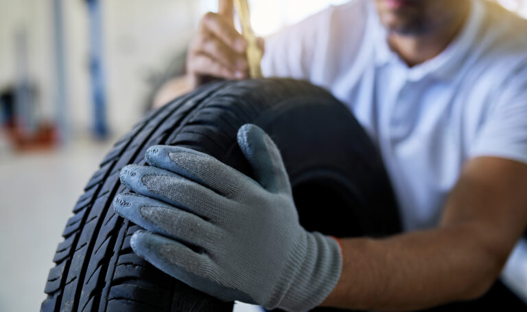 Close-up of auto repairman measuring depth of car tire in auto repair shop.